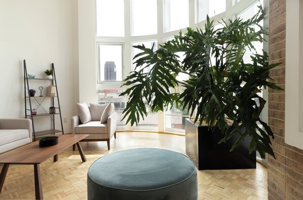 A modern living room with a sofa, ottoman, coffee table, and a large potted plant. - Balsas By Homirent (Mexico City)