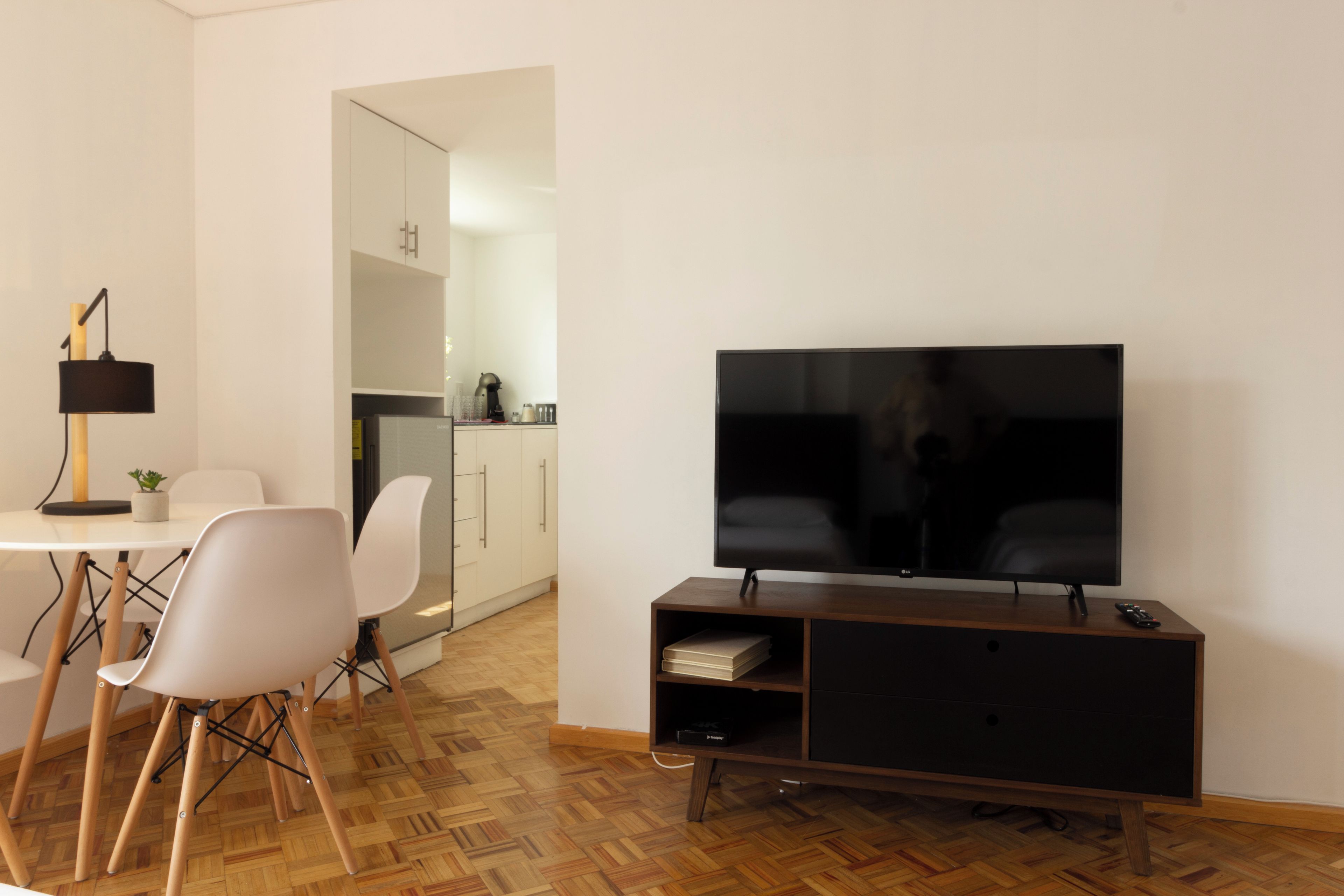 Ein modernes Wohnzimmer mit Fernseher, eine Essecke mit Stühlen und eine Küche im Hintergrund.