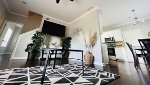 Un salon moderne doté d’un ventilateur de plafond, d’un téléviseur à écran plat et d’un coin repas agrémenté d’un tapis noir et blanc.