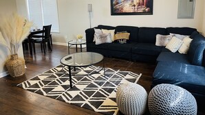 Un salon avec un canapé bleu foncé, une table basse en verre, un tapis à motifs et un tableau accroché au mur.