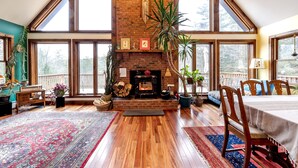 Una habitación amplia con chimenea de ladrillo, piso de madera, ventanas grandes y un comedor.