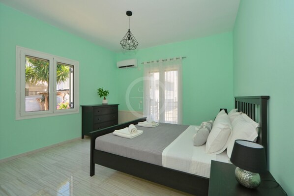 A bedroom with a bed, a dresser, a nightstand, a lamp, and a window with curtains. - A contemporary inn situated in the center of Ermioni (Ermioni)