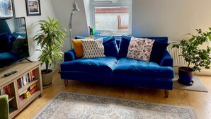 Een knusse woonkamer met een blauwe bank, een boekenkast, een televisie en een groot raam.