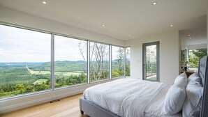Een slaapkamer met een groot raam, een bed en uitzicht op een groen landschap.