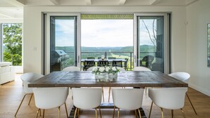 Een moderne eethoek met een grote tafel en witte stoelen, met uitzicht op een schilderachtig landschap.