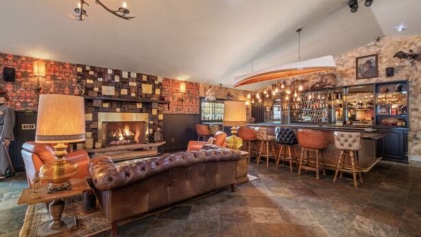 Un área de bar acogedora con chimenea, asientos de cuero y una barra con taburetes.