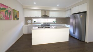 A modern kitchen with white cabinetry, a central island with a sink, a stainless steel refrigerator, and a gas stove. - Modern 6BRM House Big Group at Pakenham (Pakenham)