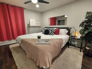 Een slaapkamer met een bed, een nachtkastje met een lamp, een spiegel en een potplant.