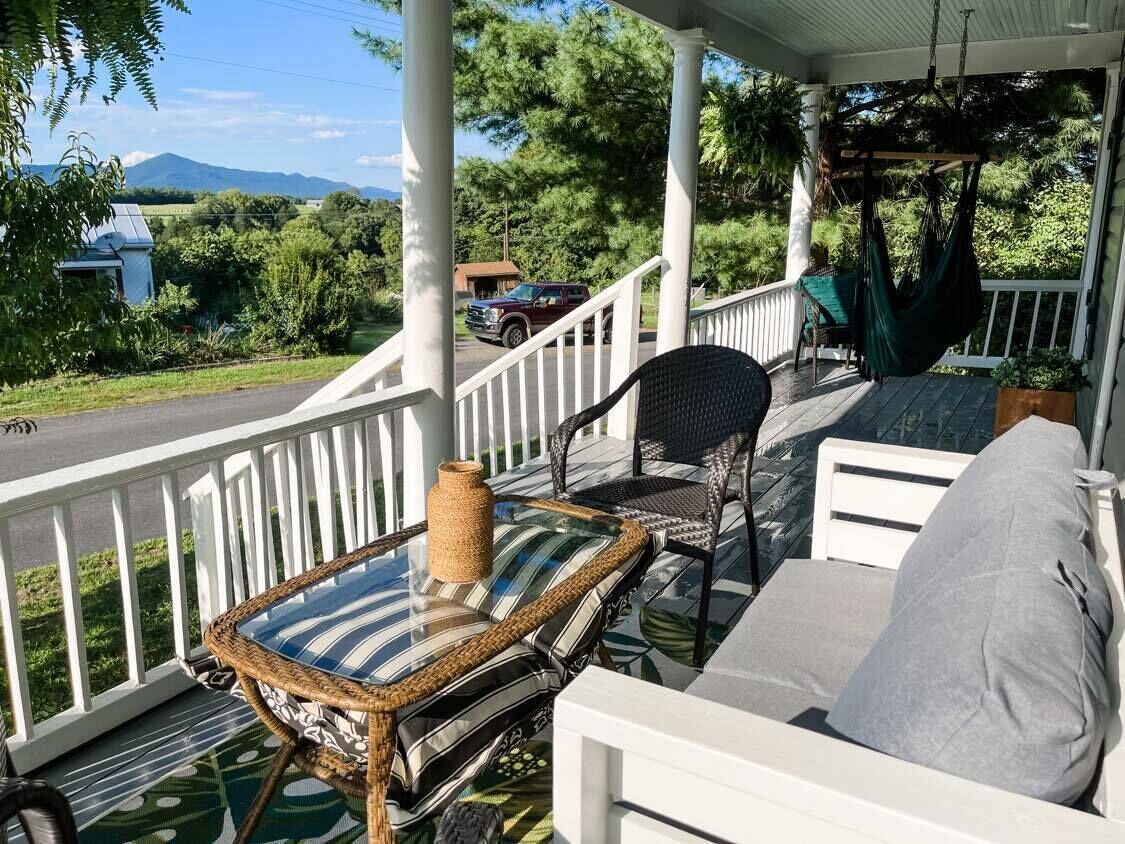 A covered porch with a wicker table and chairs, a white sofa, and a hanging chair.