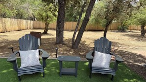 Two Adirondack chairs with white patterned cushions on a well-maintained lawn, surrounded by trees and a wooden fence. - The Flitstone Studio  (Prescott)