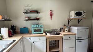 A compact kitchen with white cabinets, a blue stove, a white refrigerator, and a microwave on a shelf. - The Flitstone Studio  (Prescott)