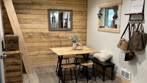 Una habitación acogedora con una pared de madera, una mesa de comedor con cuatro taburetes, un espejo y un perchero colgante.