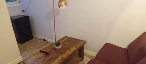 Una habitación pequeña con una mesa de madera, un sofá rojo, una pequeña planta en maceta y un armario negro.