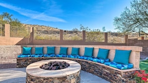 A curved outdoor seating area with a stone fire pit and blue cushions.