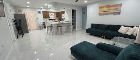 Una sala de estar moderna con un sofá verde oscuro, una mesa de centro de vidrio y un piso de mármol.