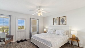 Ein Schlafzimmer mit einem Bett, einem Sessel, einem Deckenventilator und zwei Fenstern mit Jalousien.