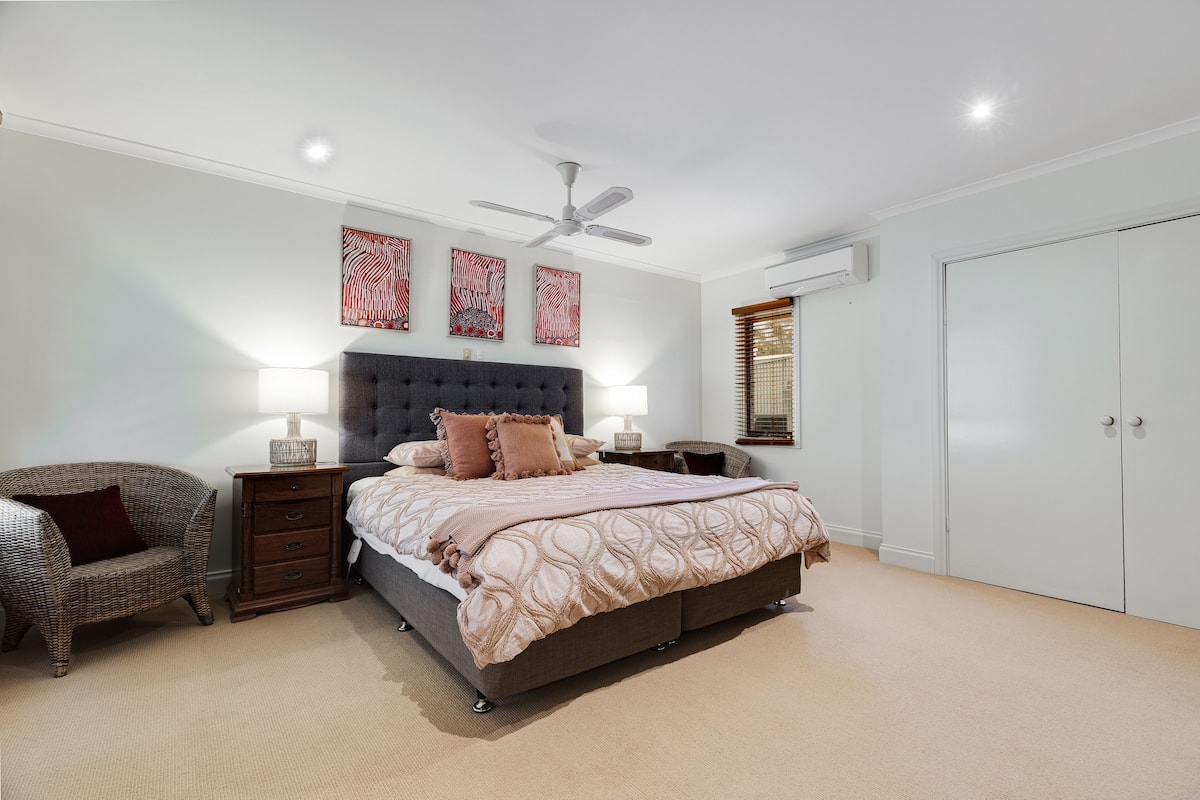 A bedroom with a bed, bedside tables, a chair, a ceiling fan, and artwork on the wall.