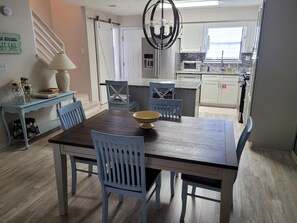 Un comedor con una mesa de madera y sillas azules, un candelabro y una cocina al fondo.