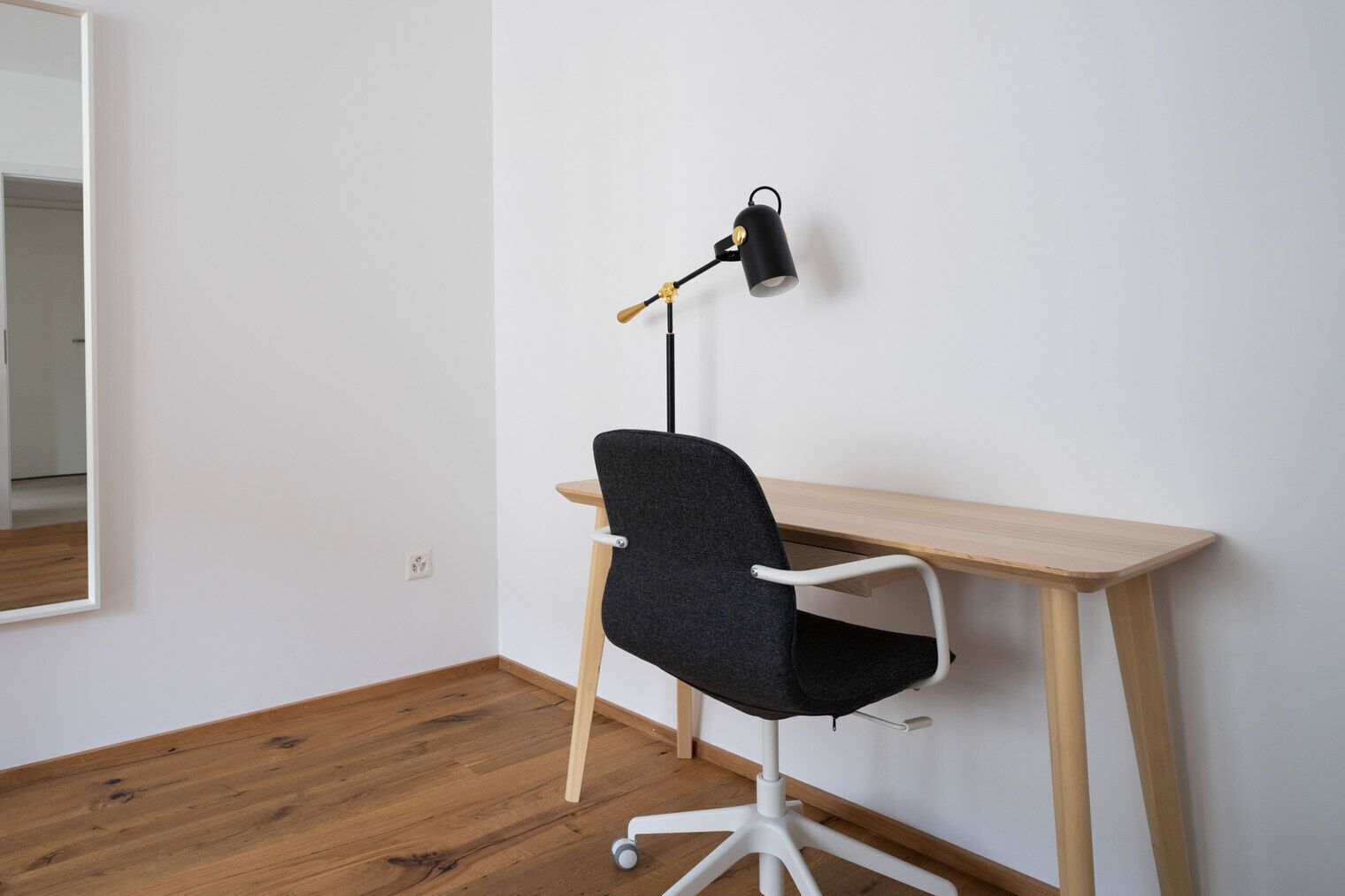 A workspace with a desk, chair, and a wall-mounted lamp.