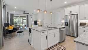 Une cuisine moderne avec des meubles blancs, un réfrigérateur en acier inoxydable et des luminaires suspendus.