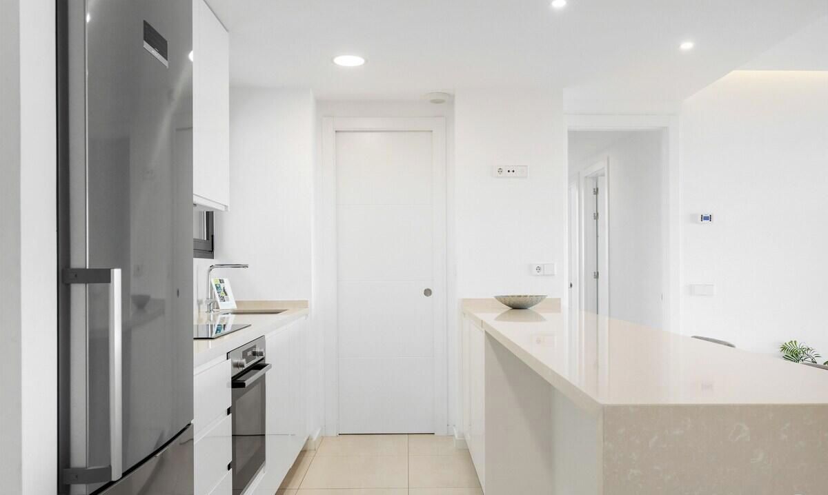 A modern kitchen with white cabinetry, a stainless steel refrigerator, a built-in oven, and a countertop with a bowl.