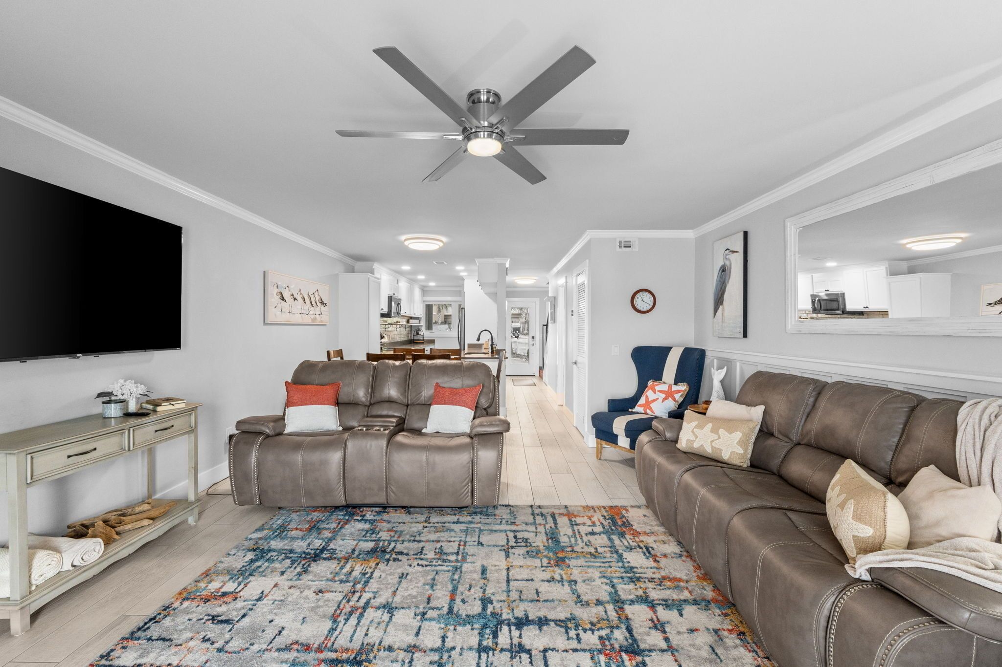 Un salon avec un ventilateur de plafond, un téléviseur, un canapé, un fauteuil et un tapis.