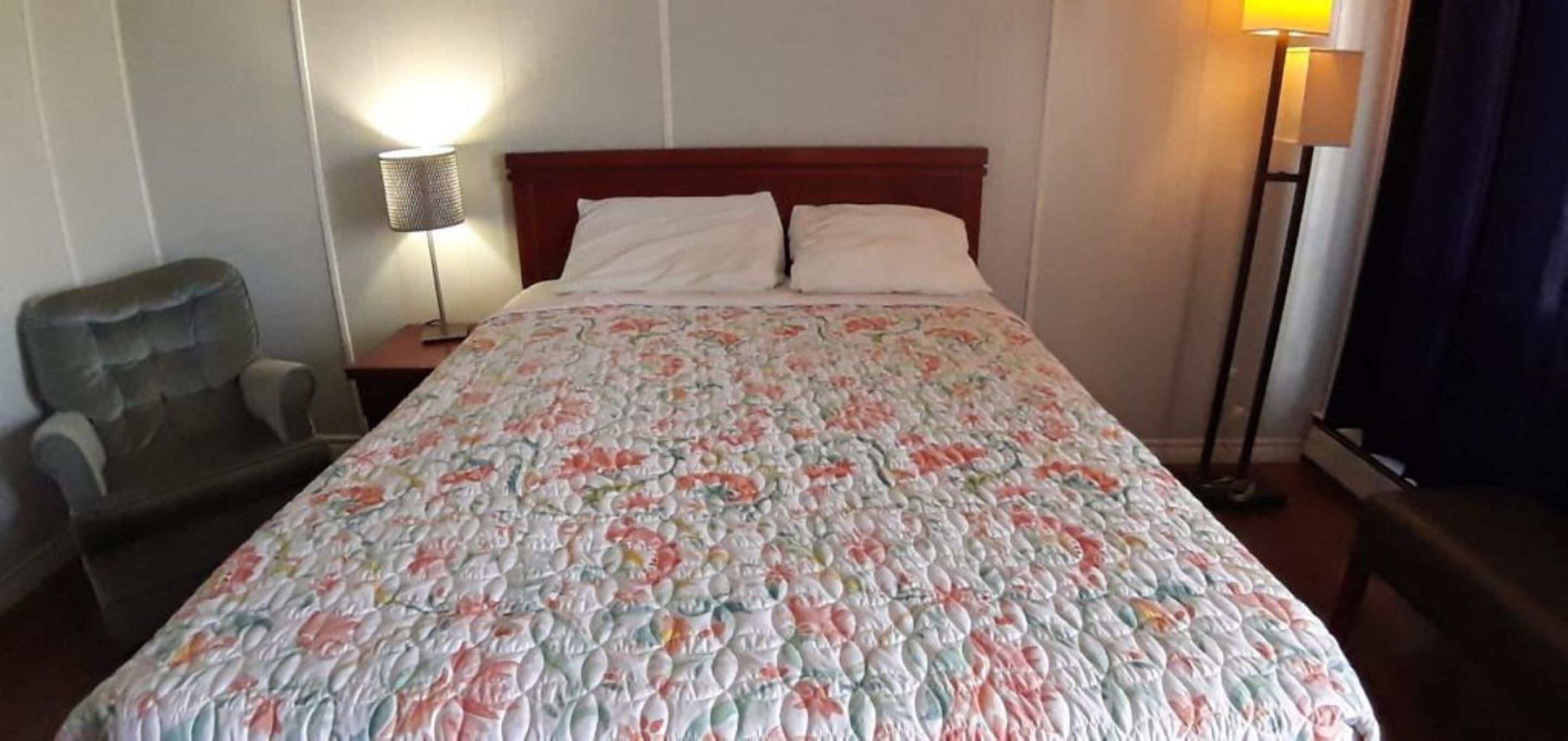 A hotel room with a bed, a chair, a nightstand, and a lamp.