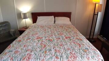 A hotel room with a bed, a chair, a nightstand, and a lamp.