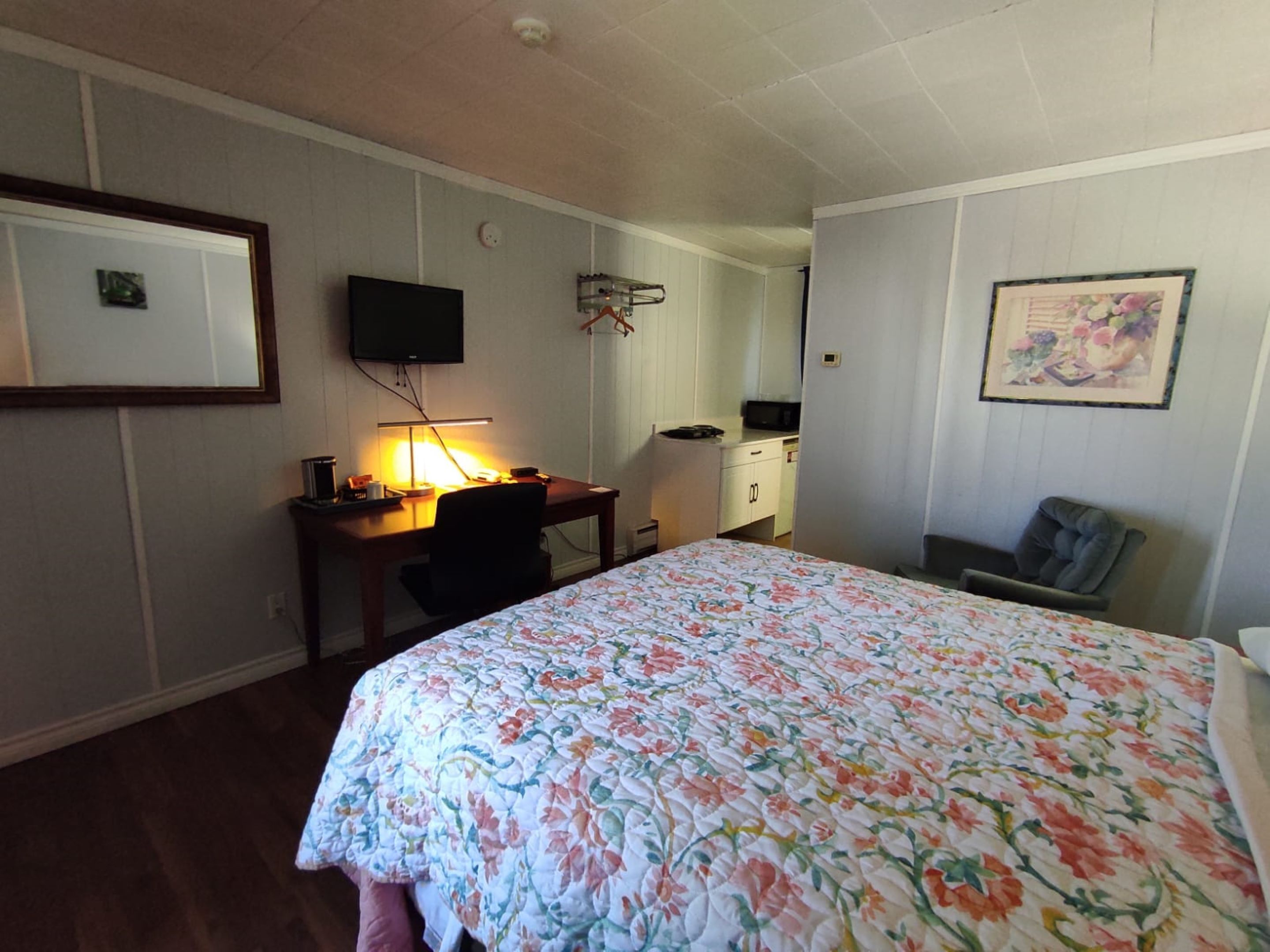 A bedroom with a bed, a desk with a lamp, a TV, and a chair.