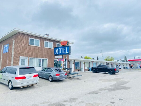A motel with a prominent 'Motel' sign, a parking lot with several cars, and a small outdoor seating area.