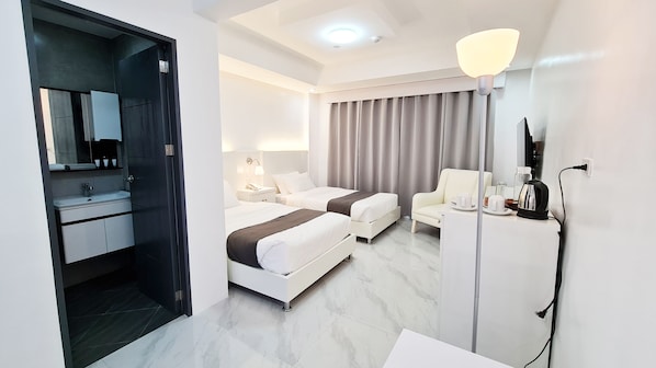 Une chambre d’hôtel équipée d’un lit, d’une table de chevet, d’une lampe, d’une chaise et d’un bureau avec une bouilloire.