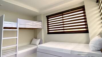 Un dormitorio con una cama litera, una cama individual, una ventana con persianas y una lámpara en el techo.