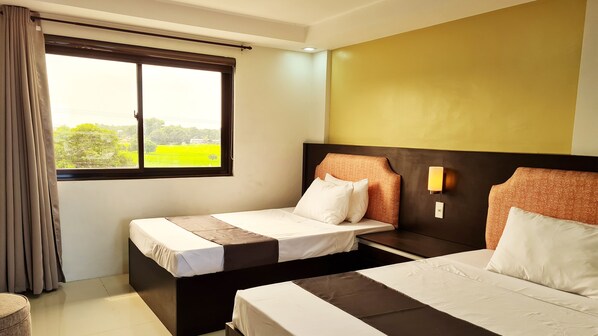 Habitación de hotel con dos camas, una ventana con cortinas, una lámpara de pared y vistas a la vegetación.