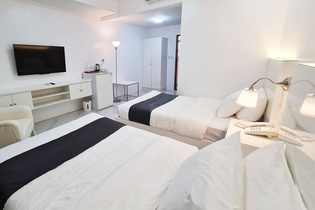 Une chambre d’hôtel avec deux lits, un bureau, une télévision, un miroir et un téléphone.