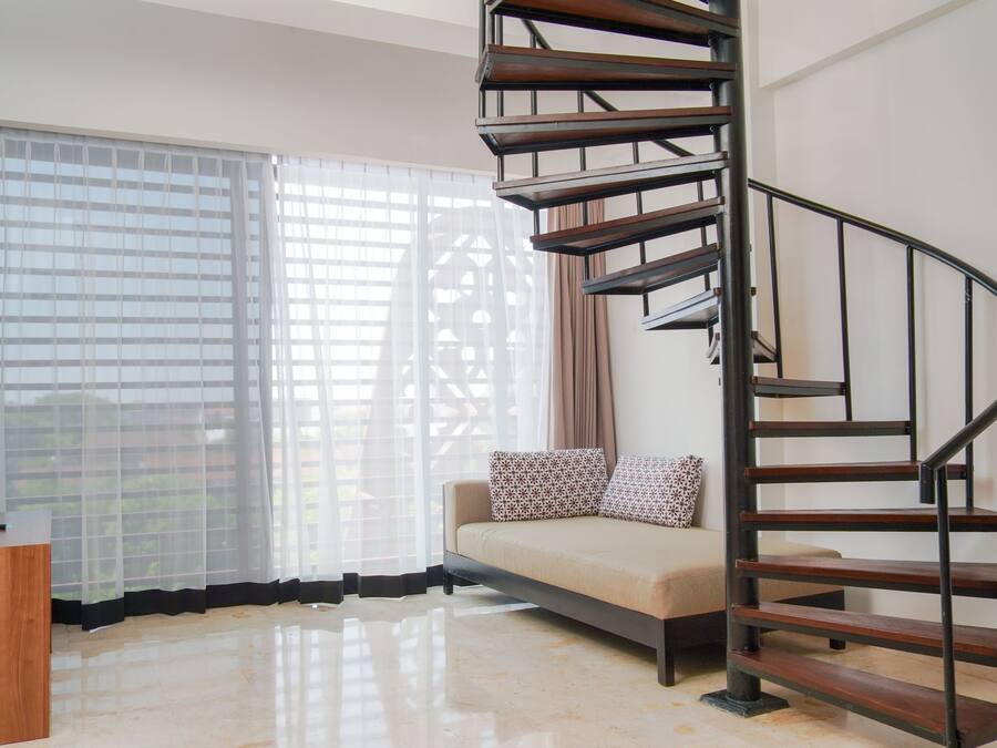 A modern living room with a spiral staircase, a sofa with patterned cushions, and a wooden desk.