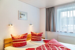 Una habitación de hotel con una cama, dos almohadas, un cuadro en la pared y una ventana con cortinas.