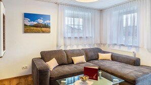 En moderne stue med en hjørnesofa, et glasbord og et landskabsmaleri.