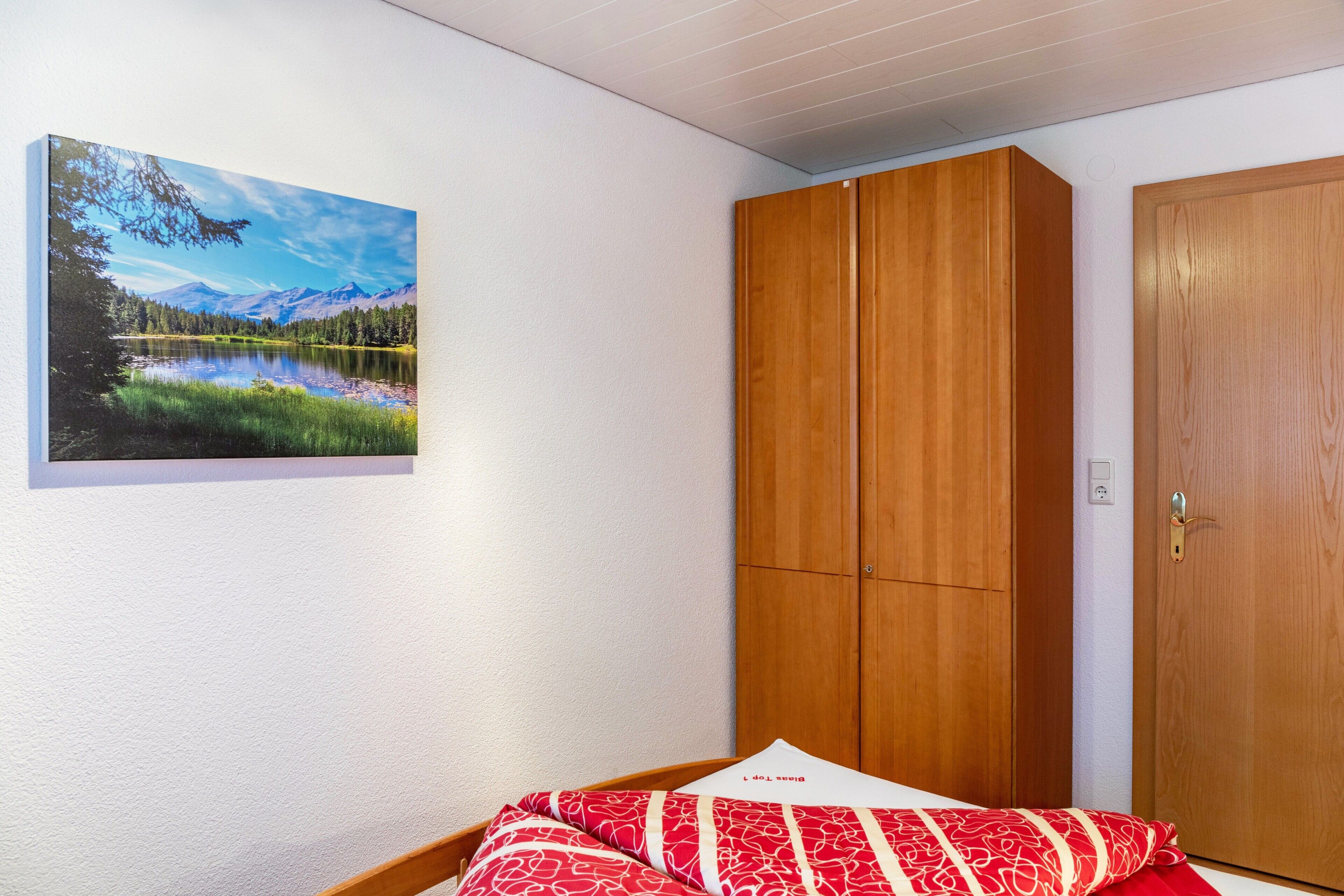Ein Schlafzimmer mit einem Bett, einem Holzschrank, einer Holztür und einem Landschaftsbild an der Wand.