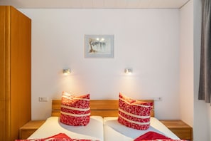 Un lit double avec des oreillers à motifs rouges, une tête de lit en bois et une petite table de chevet.