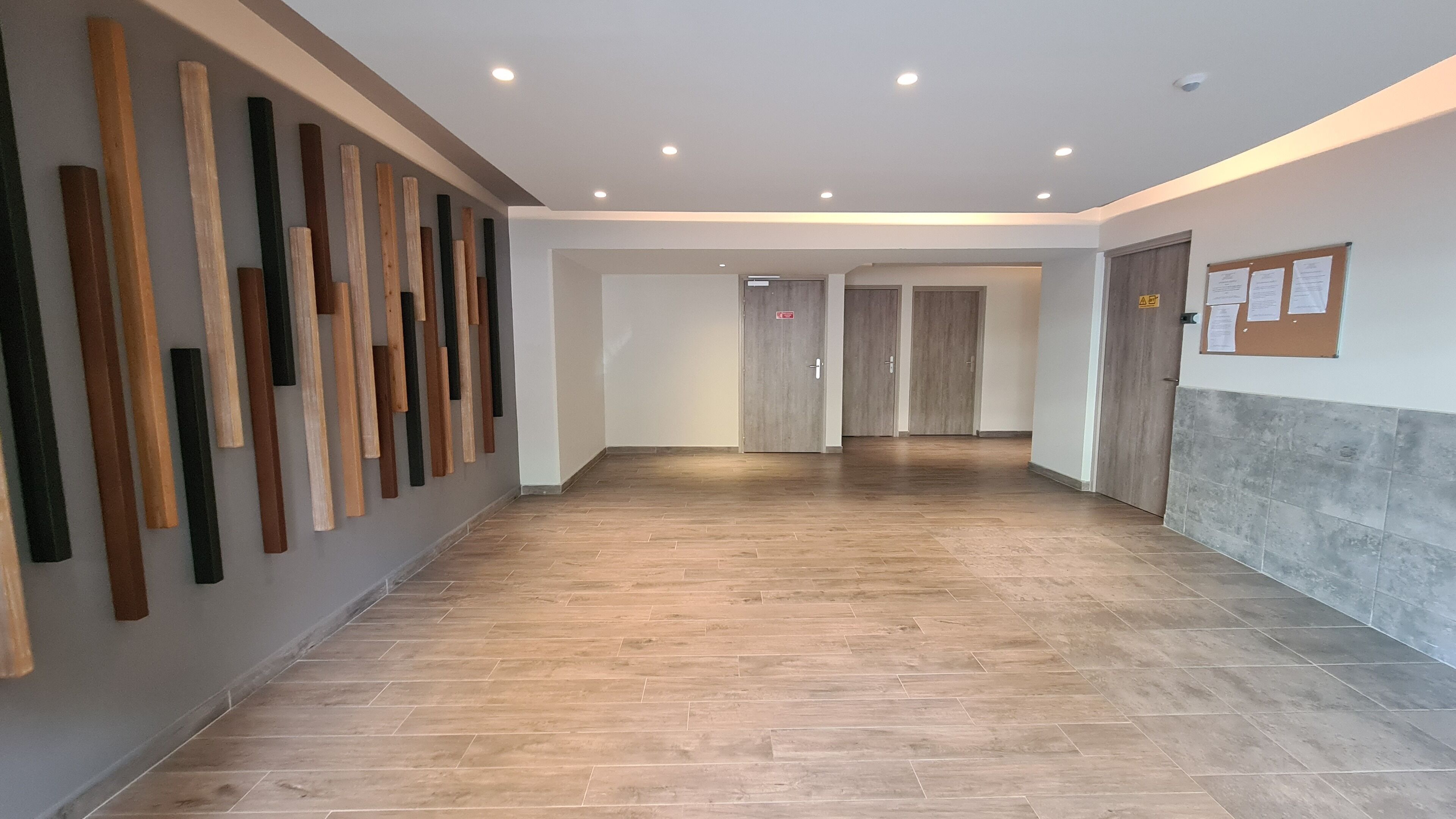 A hallway with wooden planks on the wall, a tiled floor, and doors leading to other rooms.