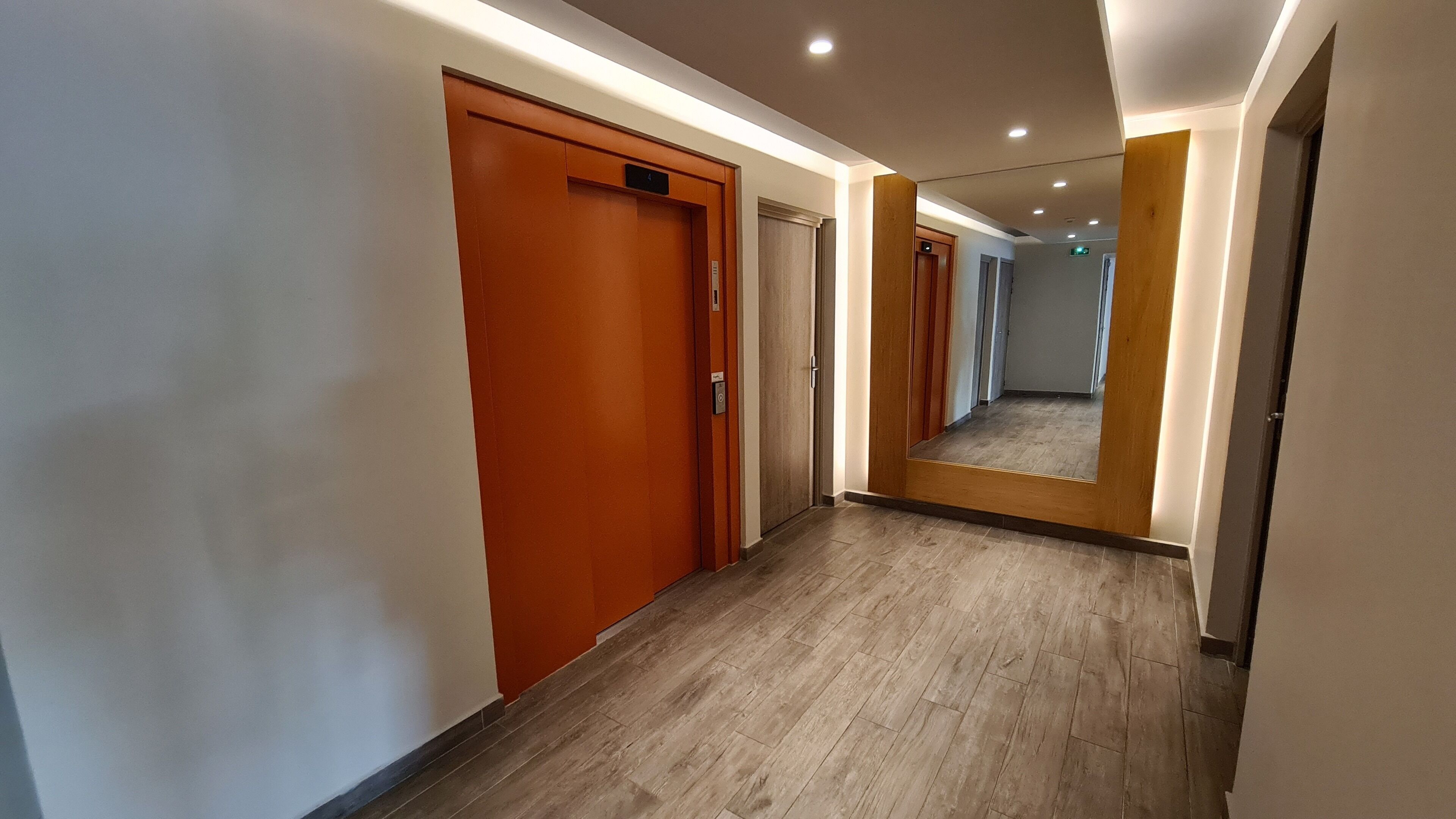Un pasillo moderno de hotel con puertas de madera, un espejo que refleja el corredor y un suelo de madera.
