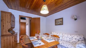 A dining area with a wooden table set for four, a floral sofa, and a wooden cabinet. - La tana dello scoiattolo central in Ski resort, Bardonecchia, Italy (Bardonecchia)