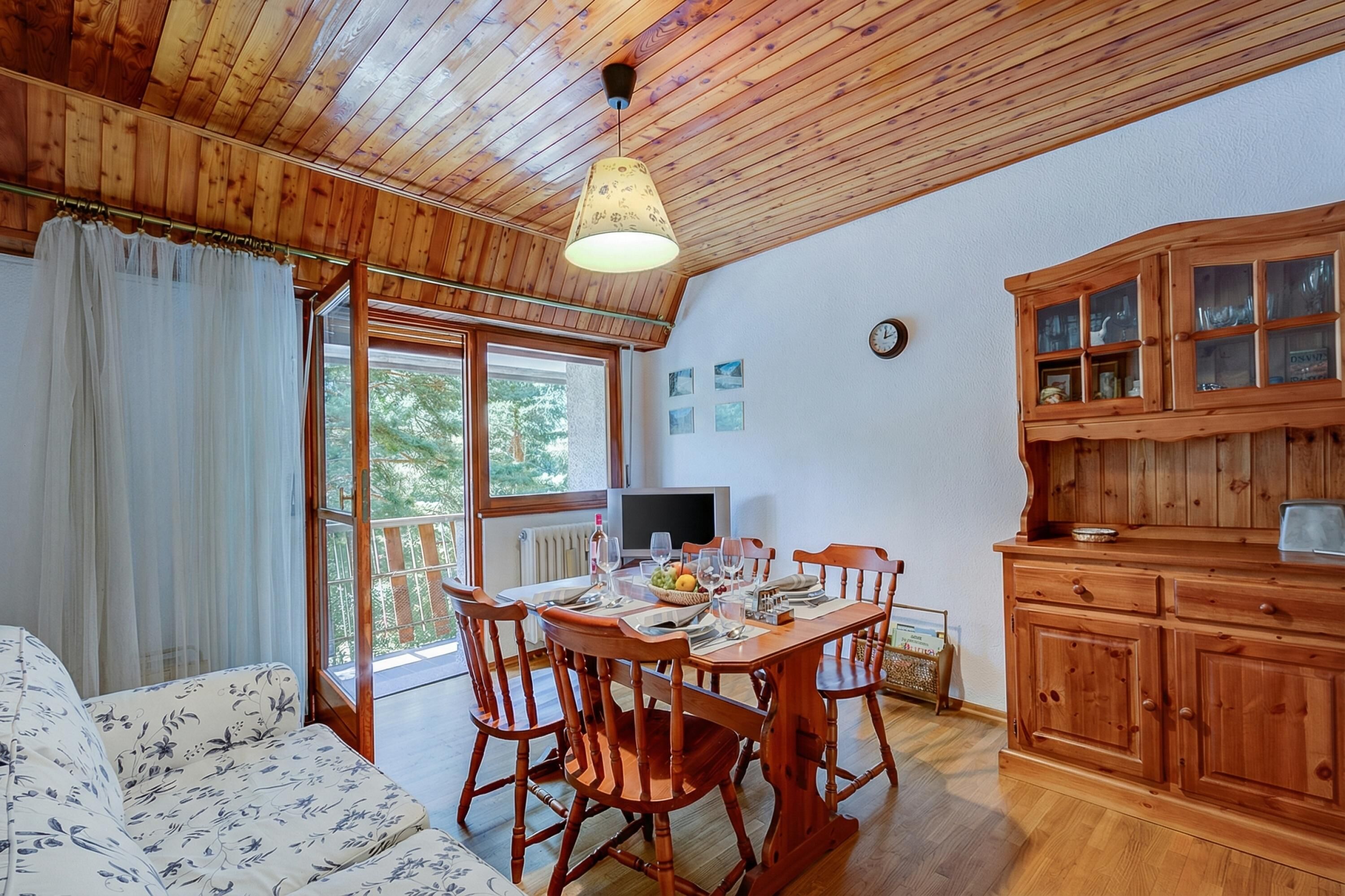 A wooden interior with a dining table set for four, wooden cabinets, and a television.