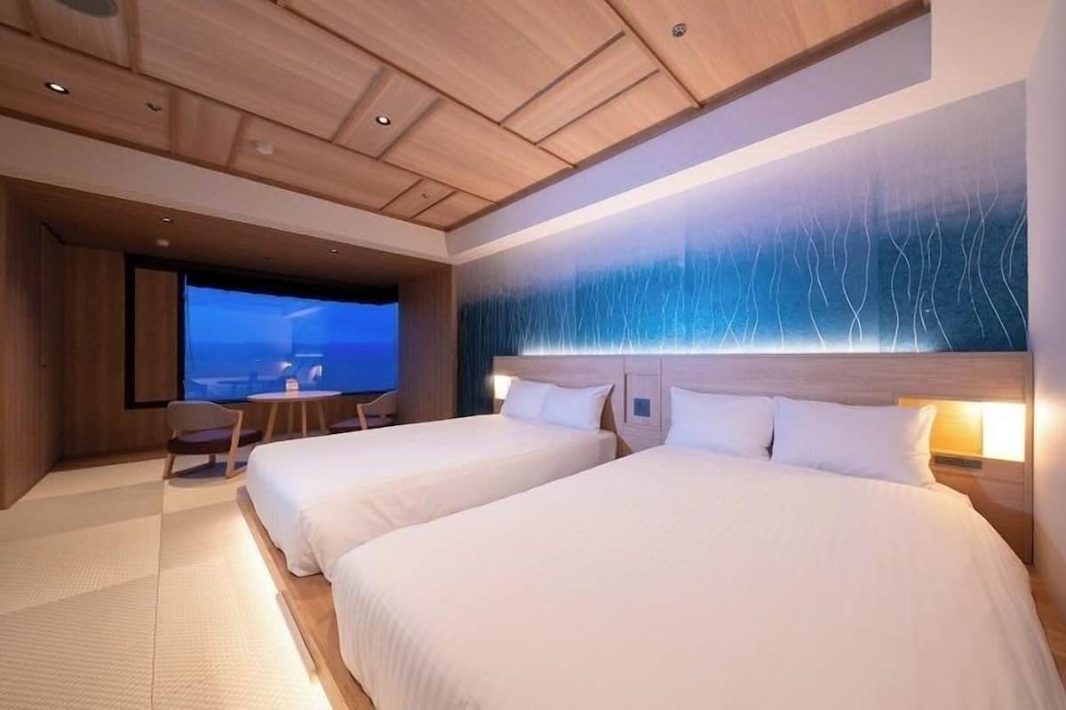 A hotel room with two beds, a desk, a chair, and a large window with a view.