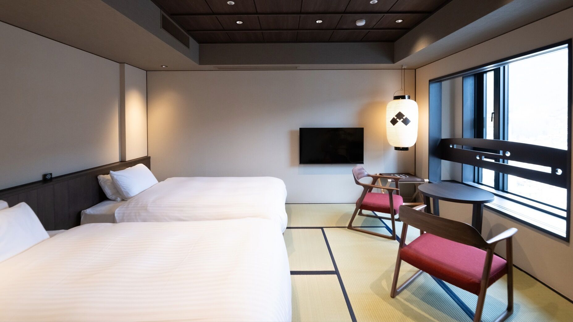 Une chambre d’hôtel avec deux lits, une télévision, une table avec des chaises et une grande fenêtre.