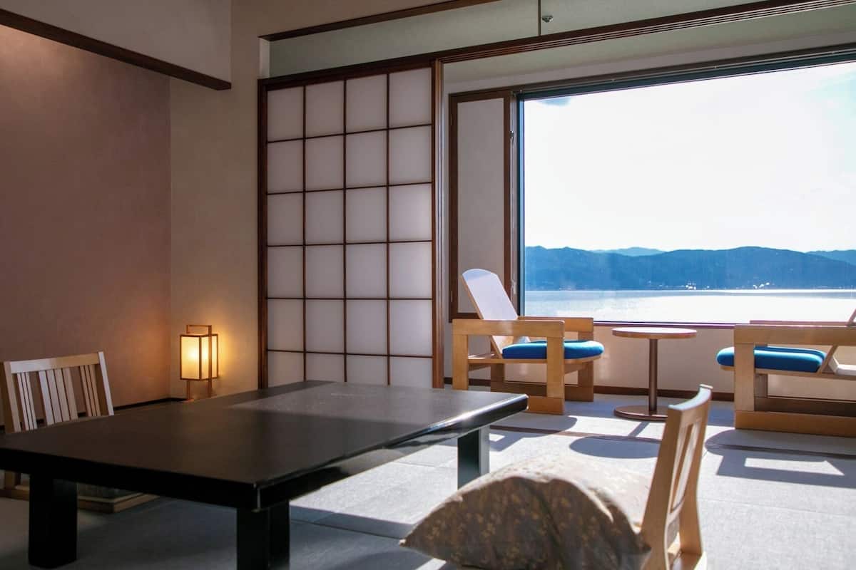 A room with a low table, two chairs, a view of a body of water, and a traditional sliding door.
