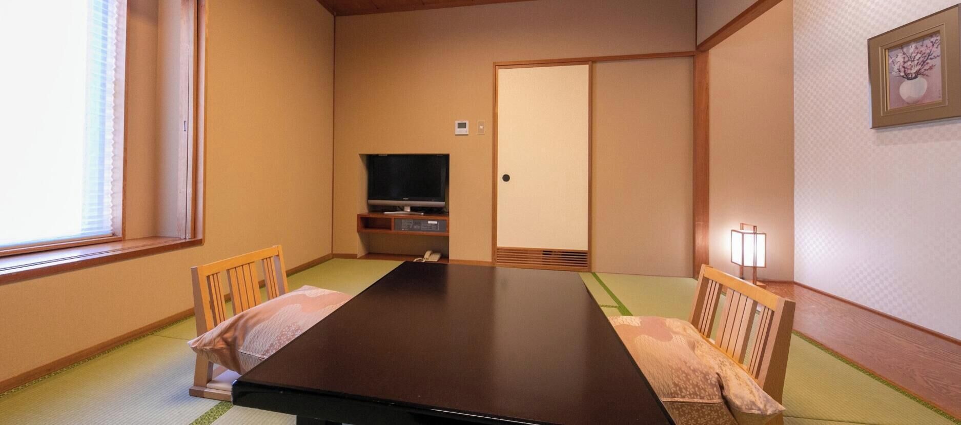 Une pièce de style japonais traditionnel, avec un sol recouvert de tatamis, une table basse et un téléviseur.