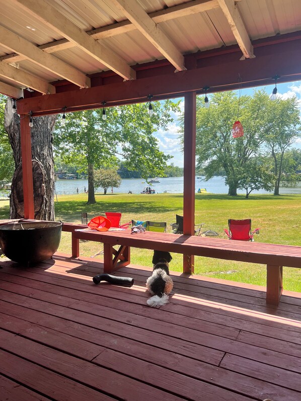Eine überdachte Terrasse mit Blick auf einen See, einem Picknicktisch und einem Hund.