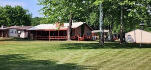 Eine rustikale Holzhütte mit Veranda, umgeben von einem gepflegten Rasen und hohen Bäumen.