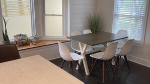 Ein Essbereich mit Tisch und Stühlen, einer Zimmerpflanze und einem Fenster mit Jalousien.